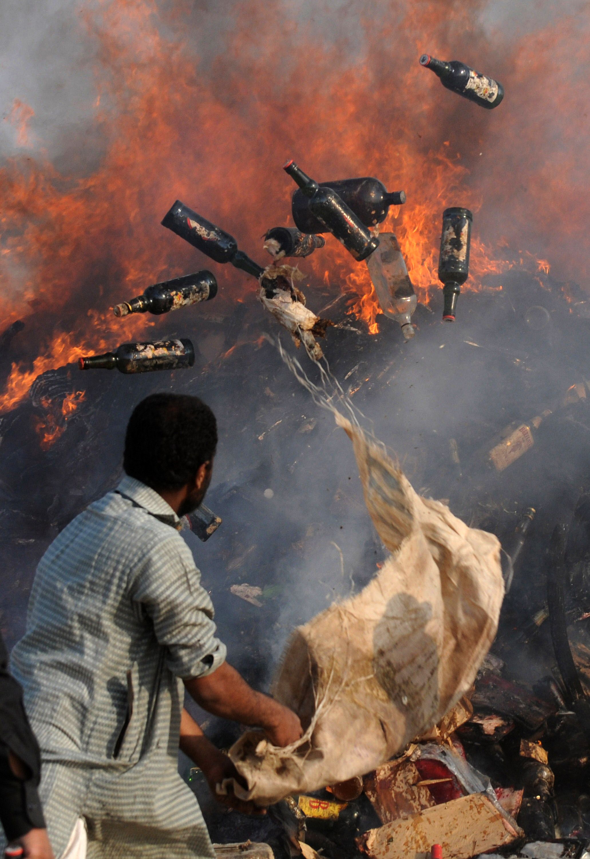 A Pakistani excise ministry official throws seized bottles of alcohol and narcotics into a fire in Karachi on February 2, 2010.  The narcotics included 105 kilograms of heroin and over 42,000 kilograms of hashish, which the authorities had confiscated during various seizures last year, which were destroyed to reiterate the country's resolve against the spread of narcotics in the South Asian nuclear-armed nation.   TOPSHOTS/AFP PHOTO/Rizwan TABASSUM